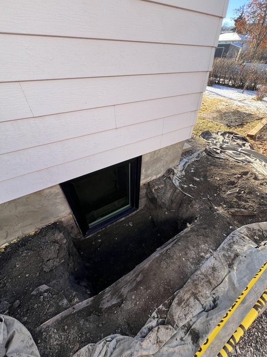 Egress window installed in winter — open excavation with snow and frost visible, Calgary